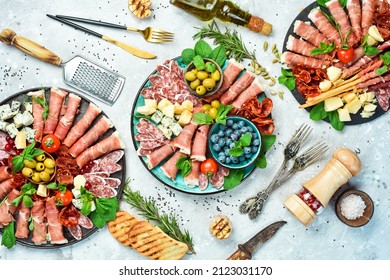 Antipasto snack set: Spanish jamon, Italian prosciutto, cheese set, olives, basil and snacks. Top view. On a gray stone background. - Shutterstock ID 2123031170