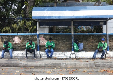 Antipolo City, Philippines - April 9, 2020: Grab food delivery drivers sit and wait on a sidewalk for orders.