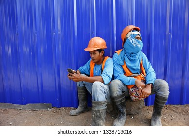 ANTIPOLO CITY, PHILIPPINES - MARCH 1, 2019: Workers at a construction site take a break and sit in front of a blue wall.