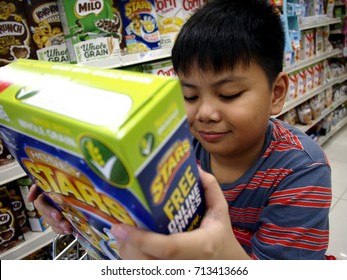 ANTIPOLO CITY, PHILIPPINES - SEPTEMBER 10, 2017: A Young Boy Reads The Label Of A Cereal Box At A Grocery Store.