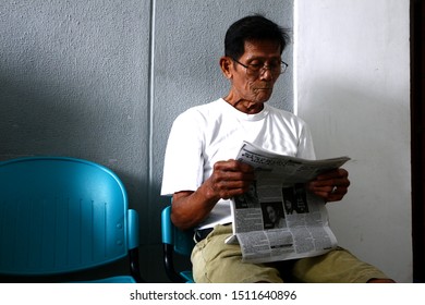 ANTIPOLO CITY, PHILIPPINES – SEPTEMBER 20, 2019: Senior Filipino Man Read Newspaper While At Waiting Area.