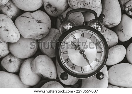 Antique alarm clock on pebbles. The concept of the passage of time. Vintage object and nature background.