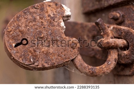 An antique almost completely rusted padlock. Completely reddish, from iron oxide (rust) old padlock that used to close the door and is still stuck in the hasp . 