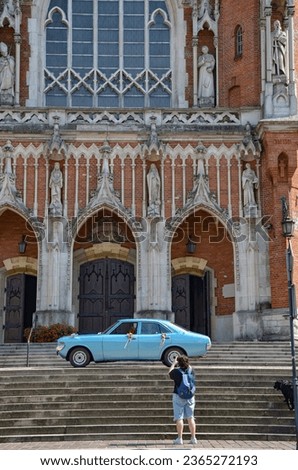 An antique blue car standing in front of the church, decorated with flowers - a wedding car and a person taking a photo
