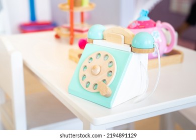 An Antique Blue Turquoise And White Rotary Home Phone Toy Made Of Wood Rests On A White Marble Patterned Shelf For Kid’s Learning And Play.