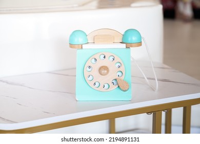 An Antique Blue Turquoise And White Rotary Home Phone Toy Made Of Wood Rests On A White Marble Patterned Shelf For Kid’s Learning And Play.