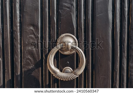 Antique brass door knocker in the shape, door element with metal knob. A old door handle on a vintage wooden black door
