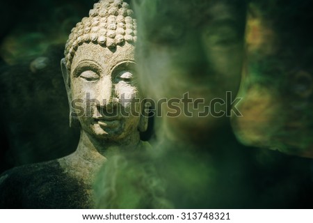 Antique buddha image statue made of stone at Umong temple , Chiang mai, Thailand under tree shade and covered by moss.