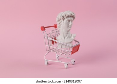 Antique bust of David with shopping trolley on a pink background. Conceptual pop. Minimal shopping still life. Creative idea