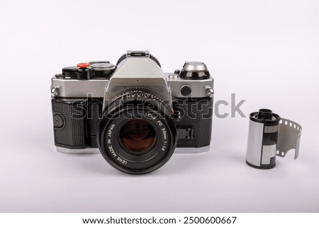 Antique camera positioned in the middle of a white backdrop, with several 35mm film rolls arranged around it. Evokes a classic photographic era.