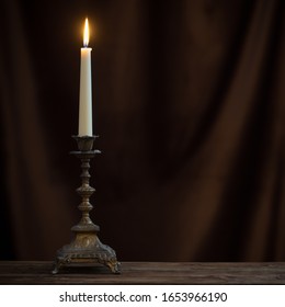 antique candlestick with burning candle on old wooden table on background brown velvet curtain - Powered by Shutterstock