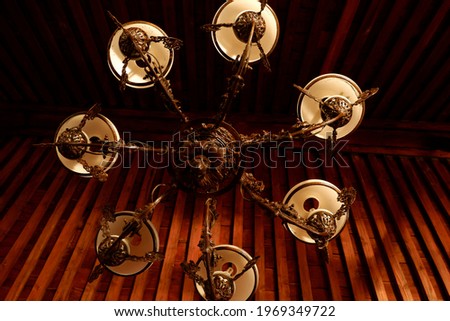 An antique chandelier with Javanese ornaments hanging from the wooden ceiling.