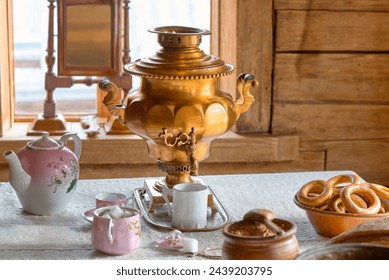 An antique copper samovar on a table in an old hut. Tea accessories on the table by the window. Preparing for tea.