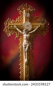 Antique crucifix of wood and gold filigran standing in front of a red velvet curtain