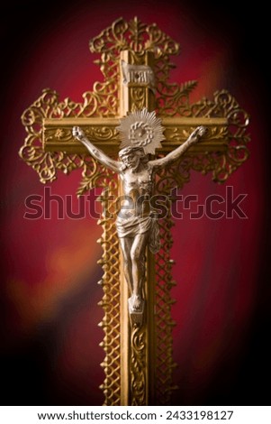 Antique crucifix of wood and gold filigran standing in front of a red velvet curtain