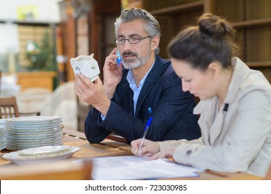 Antique Dealer Inspecting Object Assistant Making Notes Beside Him