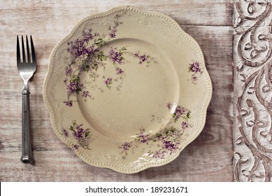 Antique decorative dinner plate (with authentic surface crazing) and vintage pewter fork on distressed wood with decorative carved border.  - Powered by Shutterstock