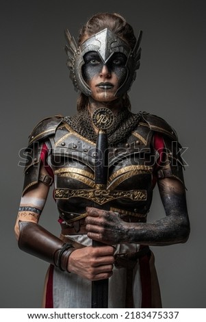 Antique female knight dressed in steel armor holding sword against dark background.