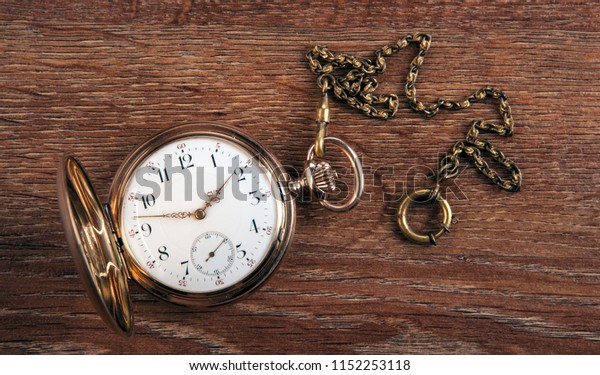 An antique gold pocket watch lies on a wooden table top\
view 