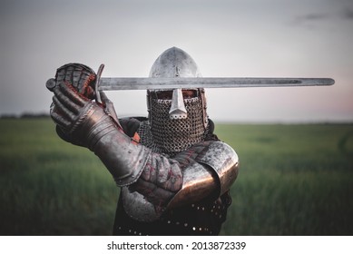 Antique knight in the plate armor and helmet holds a sword in hands close up.
