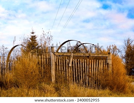 Antique metal irrigation wheels for farming sprinkler wheel lines stacked against a old wooden fence with overgrown foliage