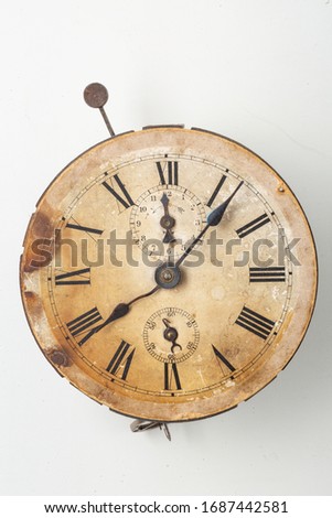 Antique object: Old withered clock of sepia colour. Roman numbers and clock face are damaged by time. Isolated object on white background.