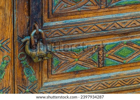 An antique padlock in the shape of a one-humped dromedary camel guards the tranquility on a beautifully decorated door with carved designs and ornaments.