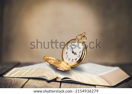 Antique pocket watch on opened old book on background.