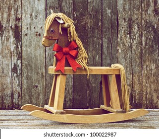 Antique rocking horse with a sparkling red Christmas bow around his neck on a rustic wooden backdrop.