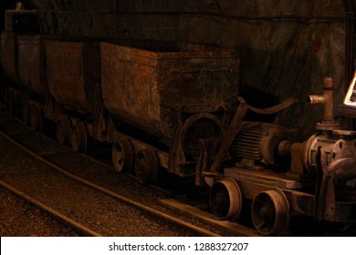 Antique And Rusted Interieur Of An Old Copper Mine Including Dark Tunnels, Tungsten Light, Rusty Wagons, Broken Wheels And Other Mining Equipment