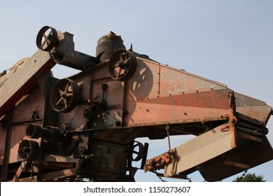 Antique rusty threshing machine side at sunset.