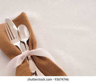 Antique Silverware Place Setting In A Brown Napkin And Tied With A Satin Ribbon Against A White Background, A Table Cloth With Room For Text Or Copy