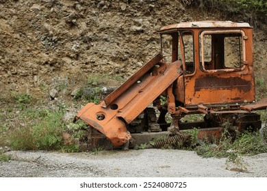 An antique tractor with rust adorning its exterior is situated in a mountainous landscape - Powered by Shutterstock