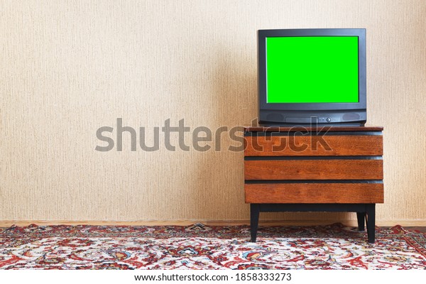 Antique TV with green screen on an antique\
wooden cabinet, old design in a house in the style of the 1980s and\
1990s.Interior in the style of the\
USSR.