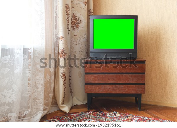 Antique TV with green screen on an antique\
wooden cabinet, old design in a house in the style of the 1980s and\
1990s.Interior in the style of the\
USSR.	