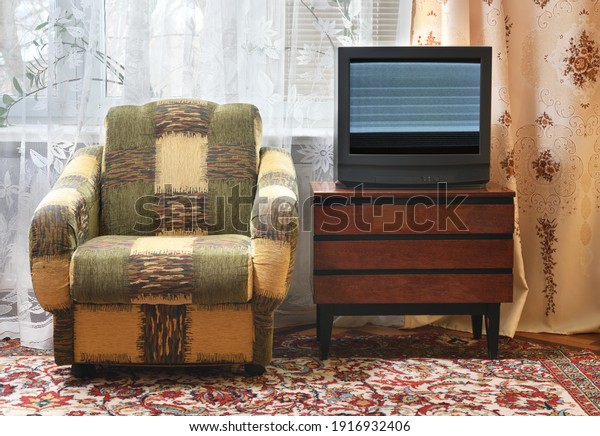 An
antique TV with static and noise on the screen sits on an old
wooden cabinet, an antique design in a house in the style of the
1980s and 1990s. Interior in the style of the
USSR.