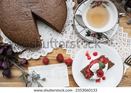 antique vintage chocolate cake with raspberry sauce and fresh raspberries on a doily and a the recipe card plus a tea cup and saucer for high tea