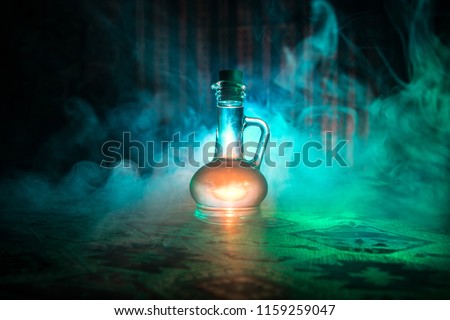 Antique and vintage glass bottle on dark foggy background with light. Poison or magic liquid concept.