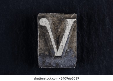 Antique vintage movable type alphabet letter V on black background.
