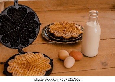An antique waffle iron with a freshly baked waffle next to it are country eggs, milk bottle and a dish with freshly baked waffles. High quality photo
