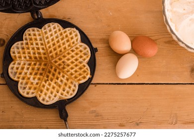 An antique waffle iron with a freshly baked waffle next to it are country eggs, milk bottle and a dish with freshly baked waffles. High quality photo