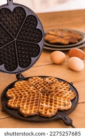 An antique waffle iron with a freshly baked waffle next to it are country eggs and a dish with freshly baked waffles. High quality photo