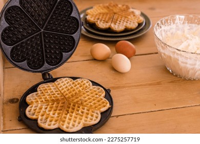 An antique waffle iron with a freshly baked waffle next to it are country eggs, a bowl of cream and a dish with freshly baked waffles. High quality photo