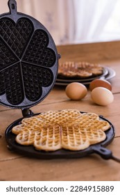 An antique waffle iron with a freshly baked waffle next to it are country eggs and a dish with freshly baked waffles. High quality photo