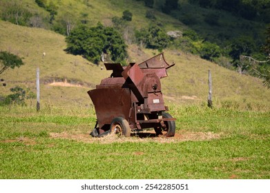 An antique wheat thresher in a rustic outdoor setting. The old agricultural machinery, with metal and wooden parts, shows vintage craftsmanship, contrasting with the natural background. - Powered by Shutterstock