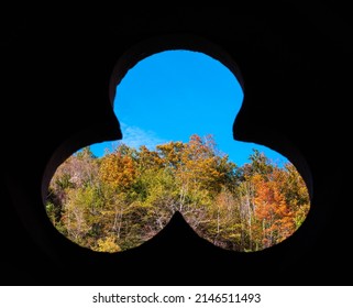 An antique window in the shape of a three-leaf clover and a view of the colorful autumn forest