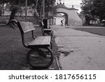 Antique wooden benches decorated with metal snakes in a park on the Kampa island in Prague, Czech Republic. Black and white monochrome image. Cyclist riding along an alley in the park against an arch.