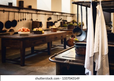 Antique XIX Century Old Kitchen With Tools, Pans, Pots And Food Ingredients All Over Che Benches And Tables