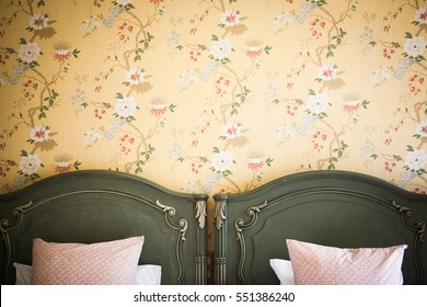 Antique yellow floral french wall paper with green wooden headboards of single beds