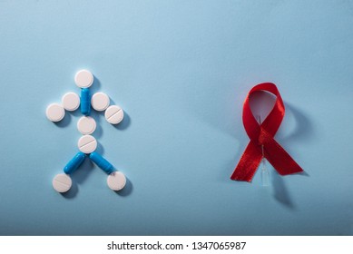 Antiretroviral Therapy For AIDS. HIV Treatment. Red Ribbon And Pills In The Form Of A Little Man On A Blue Background